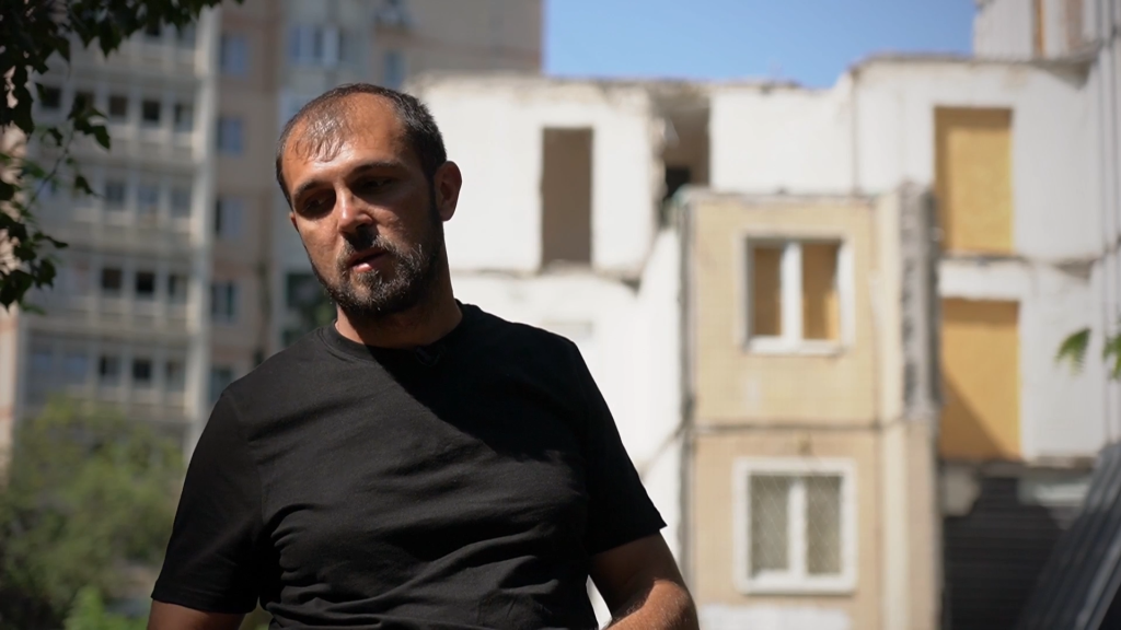 Serhiy Gaidarzhy against the backdrop of a destroyed house